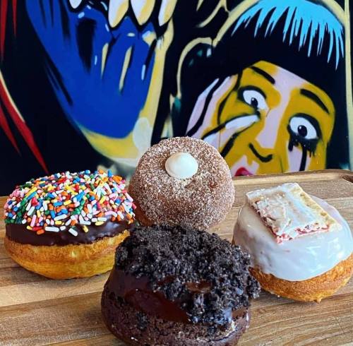 Four colorful donuts on a wooden board, with a vibrant, artistic background featuring bold, graphic designs.