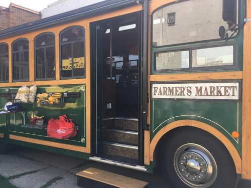 A green and wooden bus with "FARMER'S MARKET" signage, displaying fresh produce and goods outside.