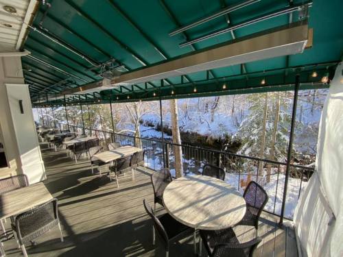 A cozy outdoor dining area with tables and chairs overlooking a snowy landscape and a stream.
