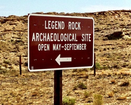 Sign for Legend Rock Archaeological Site, indicating it's open from May to September, with an arrow pointing left.