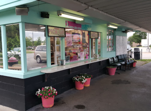 A colorful takeout window with a menu, surrounded by potted flowers and outdoor seating under a covered area.
