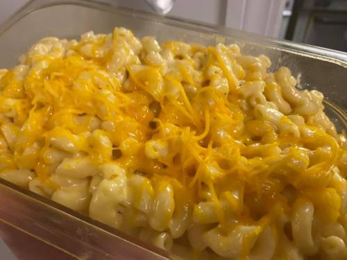 A close-up of creamy macaroni and cheese topped with shredded cheddar cheese in a clear container.