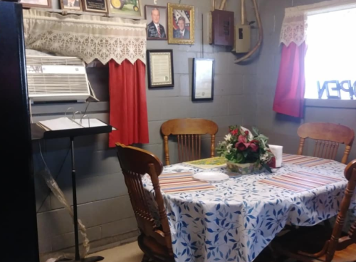 A cozy dining area with a table set for meals, surrounded by framed photos and decorative curtains.
