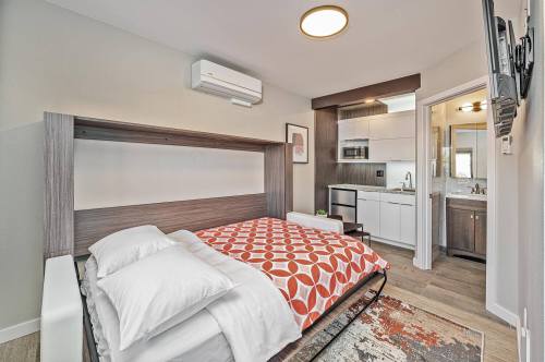 Cozy bedroom with a foldable bed, orange patterned blanket, kitchenette, and modern decor.