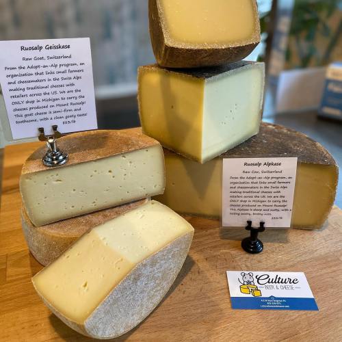 Assorted Swiss cheeses displayed on a wooden board with informational signs and a business card.
