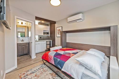 Cozy bedroom with a foldable bed, colorful bedding, and a kitchenette area, featuring modern decor and natural light.