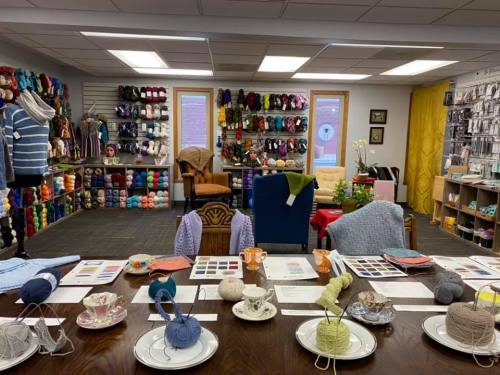 A cozy yarn shop with colorful yarn displays, a crafting table, and seating areas for creativity and inspiration.