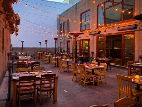 Outdoor restaurant patio with string lights, tables set for dining, and heaters, creating a cozy evening atmosphere.