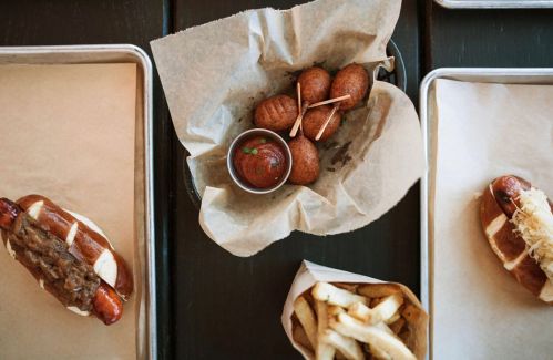 A top-down view of a meal featuring hot dogs, cornbread balls, and fries on parchment-lined trays.