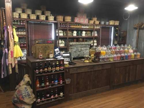 A rustic store interior featuring wooden shelves filled with jars of candy, drinks, and various vintage items.