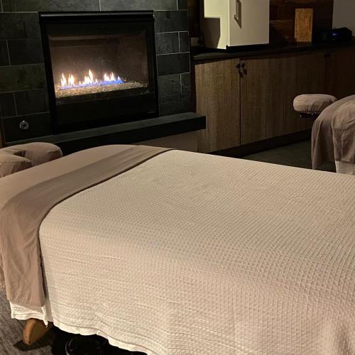 A cozy spa room with a massage table and a fireplace in the background, creating a relaxing atmosphere.