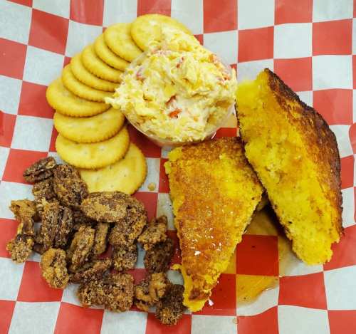 A plate with cornbread, pimento cheese dip, crackers, and candied pecans on a red and white checkered background.