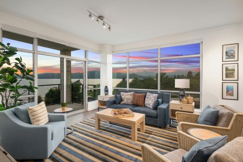 Cozy living room with large windows showcasing a sunset view, featuring modern furniture and a warm color palette.