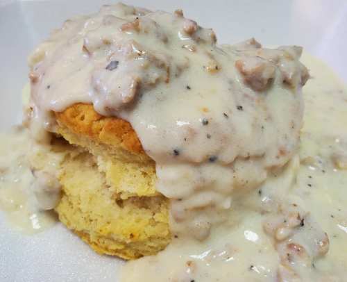A fluffy biscuit topped with creamy sausage gravy, served on a white plate.