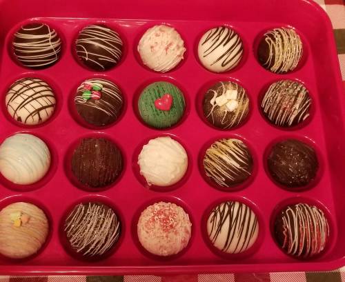 A tray of assorted decorative chocolates in various colors and designs, arranged in a pink container.