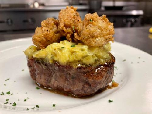 A plated dish featuring a meatloaf topped with fried shrimp and a layer of sautéed cabbage, garnished with herbs.