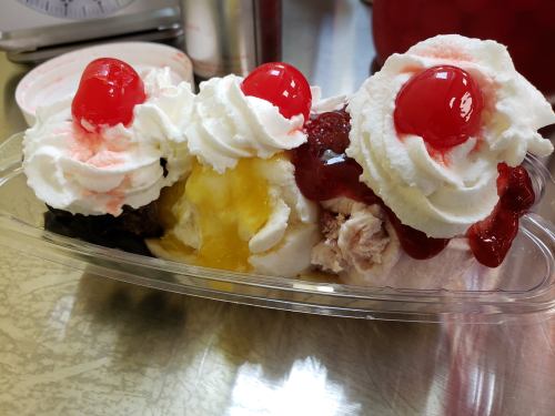 A dessert dish with three scoops of ice cream topped with whipped cream and cherries, served in a clear container.
