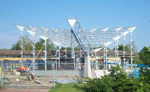 A partially constructed building with a unique roof design, surrounded by scaffolding and construction equipment.