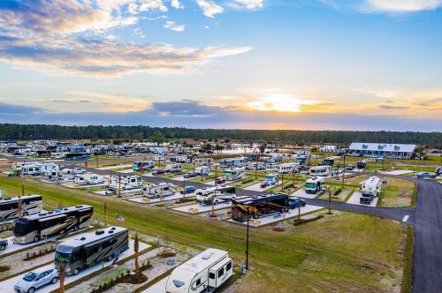 Aerial view of a large RV park at sunset, with numerous parked RVs and a scenic landscape in the background.