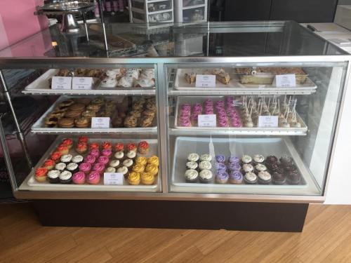 A display case filled with various colorful cupcakes, cookies, and desserts, each labeled with prices.