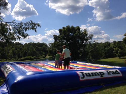 A colorful inflatable jump pad with children playing on it, set against a sunny sky and green trees.