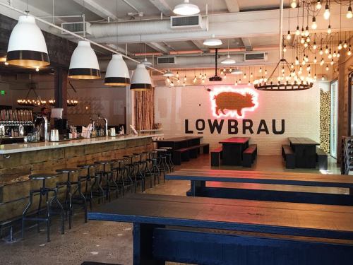 Interior of a modern restaurant with wooden tables, a bar, and a neon pig sign on the wall. Warm lighting creates a cozy atmosphere.