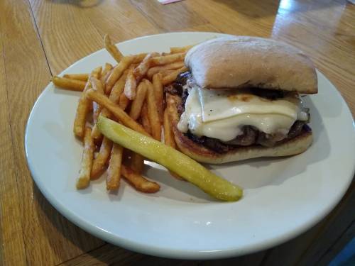 A plate with a sandwich featuring melted cheese and grilled meat, accompanied by golden fries and a pickle.