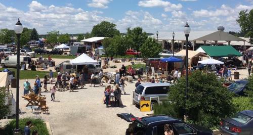 A bustling outdoor market with vendors, tents, and crowds enjoying a sunny day.