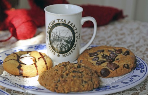 A plate with three types of cookies next to a mug featuring the Boston Tea Party Ships & Museum logo.