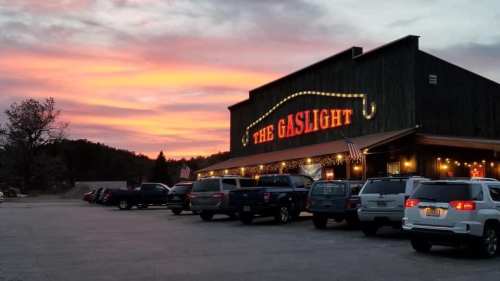 A rustic building with "The Gaslight" sign, surrounded by parked cars, under a colorful sunset sky.