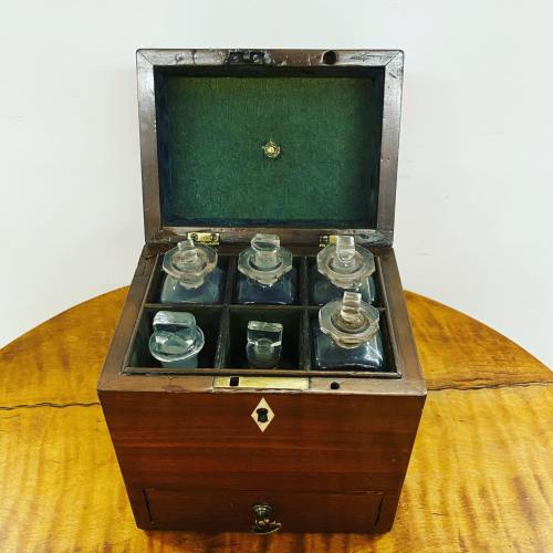 A wooden box with a green interior, containing six glass bottles, sits on a round wooden table.
