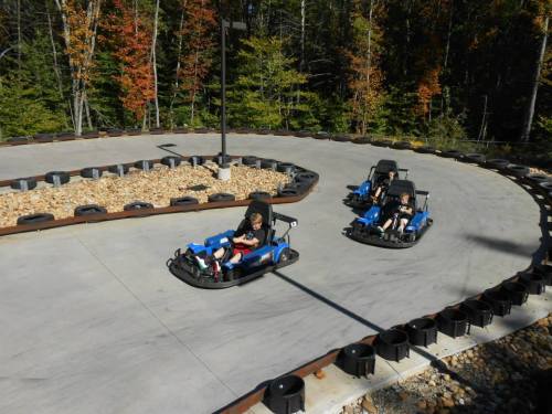Two go-karts racing on a winding track surrounded by trees with autumn foliage.