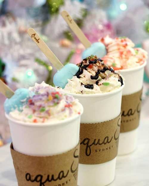 Three cups of colorful ice cream topped with sprinkles and sauces, set against a festive background.