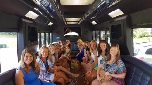 A group of smiling women sitting inside a party bus, dressed in colorful outfits, enjoying a fun outing together.