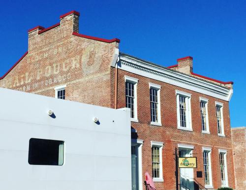 Historic brick building with a faded sign, blue sky, and a modern white structure in front.