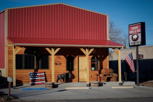 A rustic wooden building with a red metal roof, featuring an "Open" sign and an American flag outside.