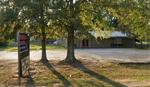 A diner building surrounded by trees, with a sign in front and a gravel parking area.