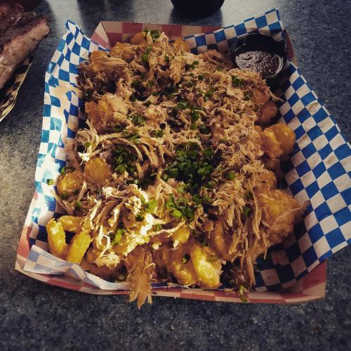 A basket of loaded tater tots topped with pulled pork, green onions, and a side of barbecue sauce.