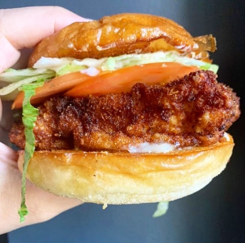 A hand holding a crispy fried chicken sandwich with lettuce and tomato on a toasted bun.