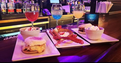 A colorful display of drinks and dishes, including sliders, bacon, and dessert, on a bar counter.