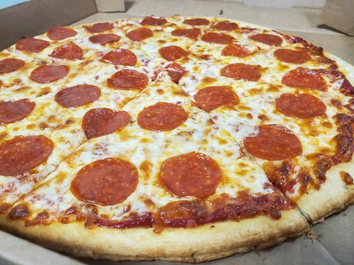 A large pepperoni pizza with melted cheese and a golden crust, partially sliced in a cardboard box.