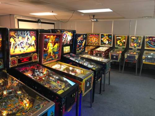 A row of colorful pinball machines in a well-lit arcade room.