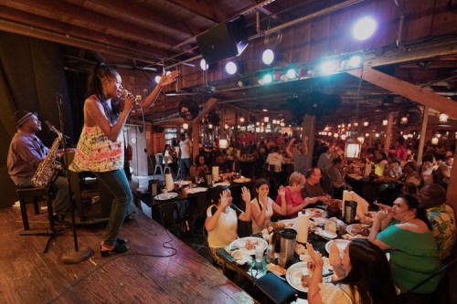A lively restaurant scene with a singer performing on stage while diners enjoy their meals and engage with the performance.