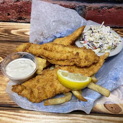 Fried fish fillets with a lemon wedge, coleslaw, and dipping sauce on a wooden table.