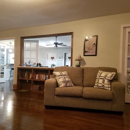 Cozy living room with a sofa, decorative pillows, and a bookshelf, featuring a doorway to another room in the background.