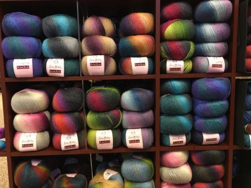 A display of colorful yarn skeins stacked neatly on shelves, showcasing various shades and patterns.