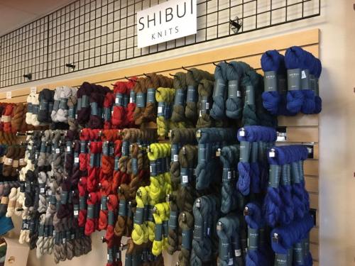 A colorful display of Shibui Knits yarn in various shades, neatly arranged on a wall.