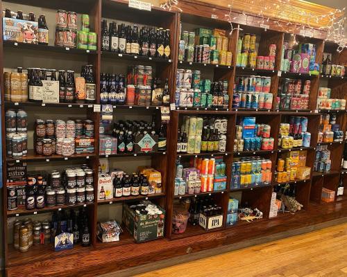 A wooden shelf displaying a variety of beer bottles and cans in different colors and brands.