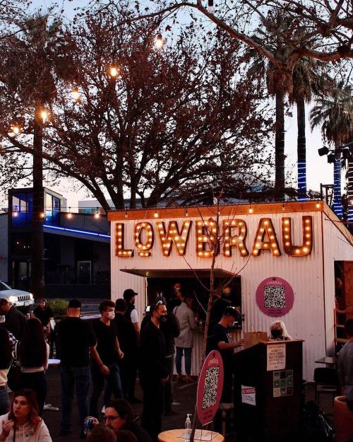 A lively outdoor scene at Lowbrau, with string lights, palm trees, and people enjoying the atmosphere.