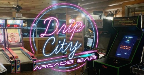 Neon sign for "Drip City Arcade Bar" with arcade games and a skee-ball machine in a cozy interior setting.